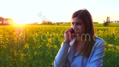 年轻漂亮的女人用智能手机在夕阳田野的剪影上。